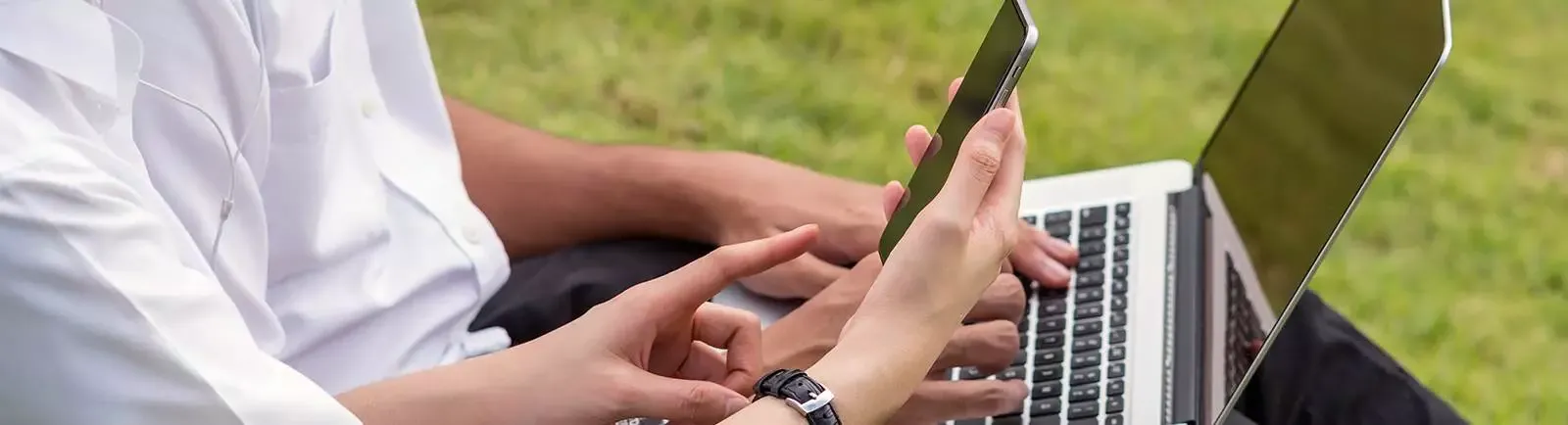 close up on two sets of hands, one holding a phone and one holding a laptop