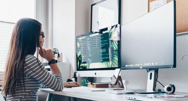 woman working at a desk using two computer monitors